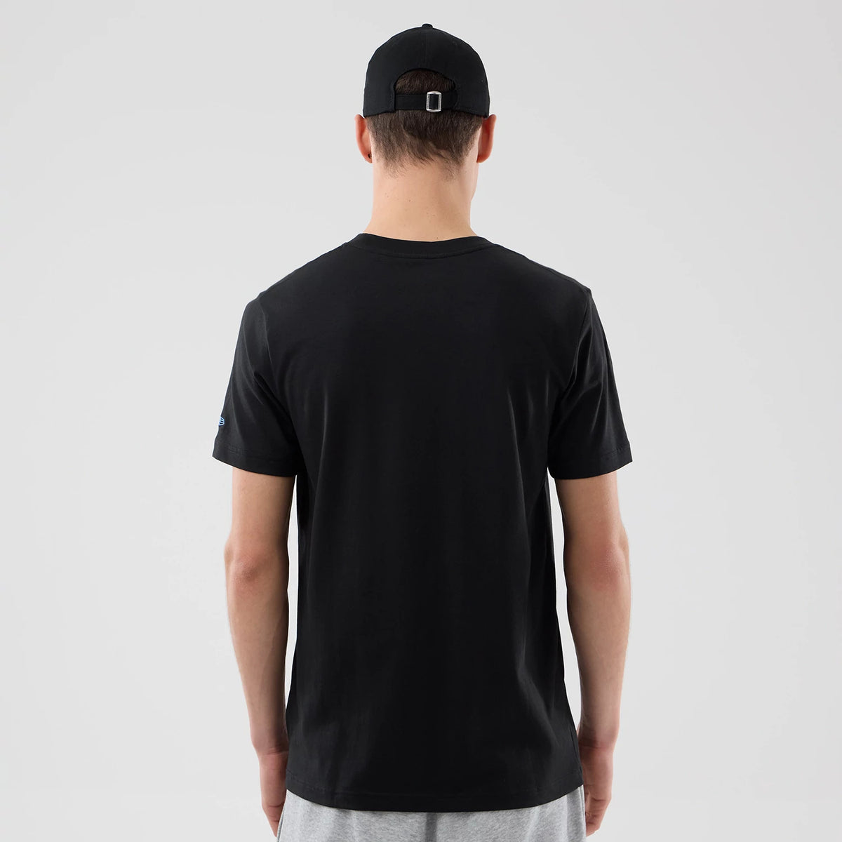 New Era Chicago Bulls NBA City Edition Black T-Shirt, back view on-model showing the plain black back with short sleeves, a small embroidered logo on the left sleeve, and a matching black cap worn by the model.