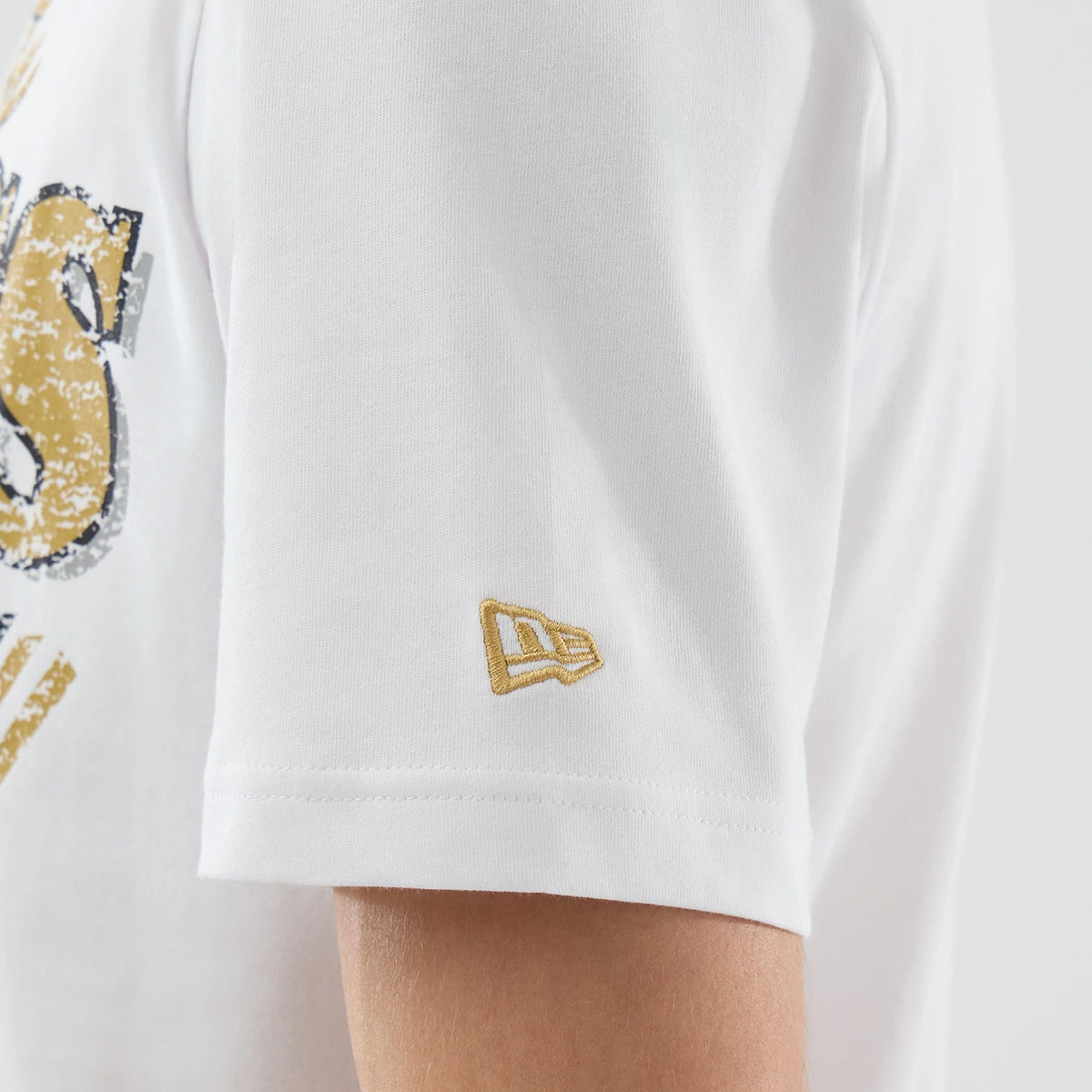 New Era Boston Celtics NBA City Edition White T-Shirt, side view showing a detailed close-up of the sleeve with a gold embroidered New Era logo and part of a distressed gold graphic on the body of the shirt.