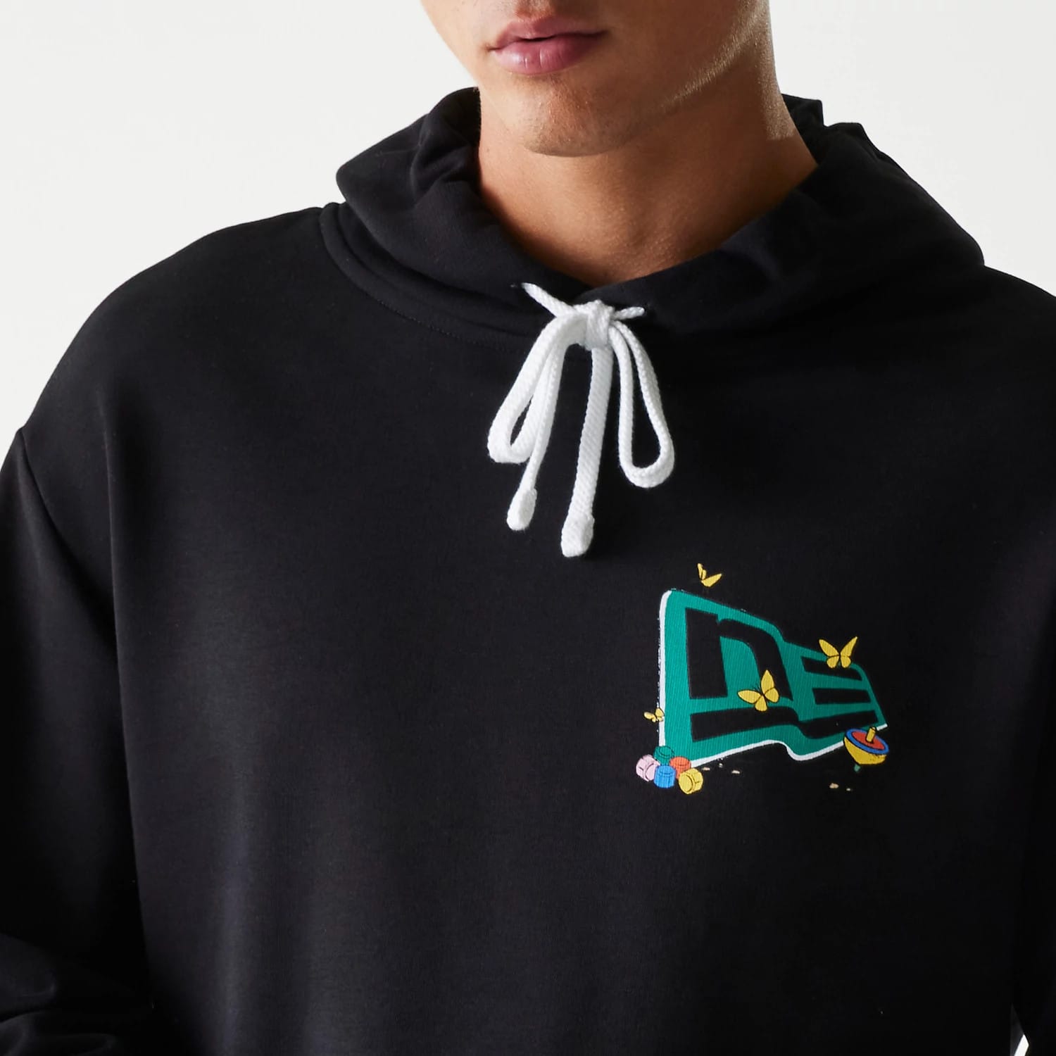 New Era Netflix Squid Game Black Oversized Pullover Hoodie, front view on-model showing white drawstrings at the neck and a colourful embroidered design with floral elements on the left chest.