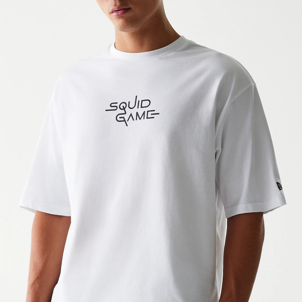 New Era Netflix Squid Game White Oversized T-Shirt, front view on a model showing the Squid Game text logo printed in the centre of the chest and a small embroidered New Era logo on the sleeve.