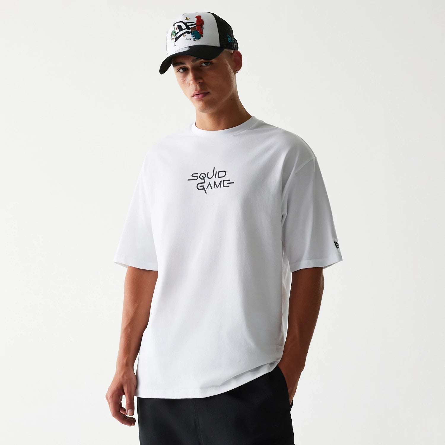 New Era Netflix Squid Game White Oversized T-Shirt, front view on a model with a black and white cap, featuring the Squid Game logo printed in black on the centre chest and a small embroidered New Era logo on the sleeve.