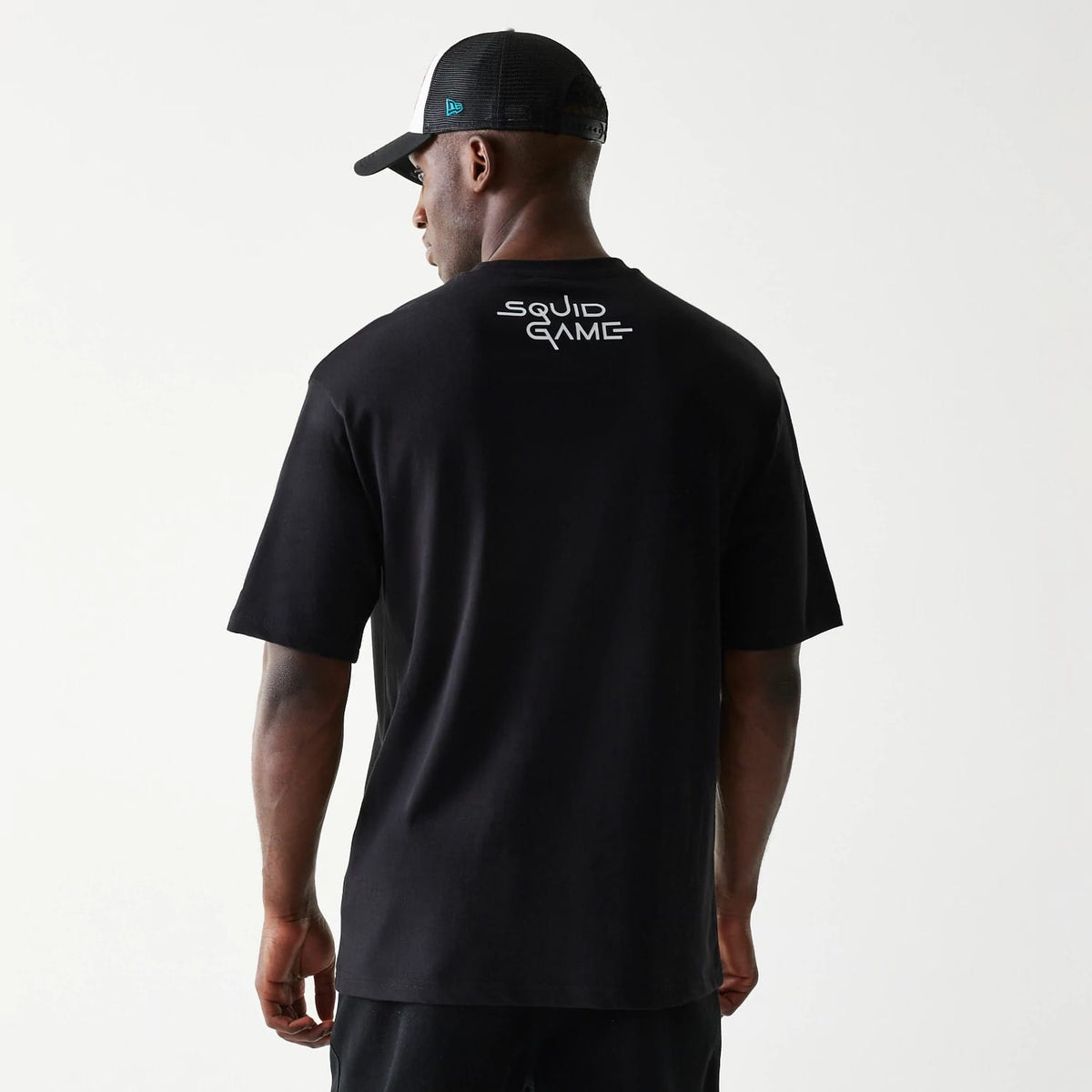 New Era Netflix Squid Game Black Oversized T-Shirt, back view on a model showing the white Squid Game lettering centred near the top on a plain black fabric, with short sleeves and a relaxed fit.
