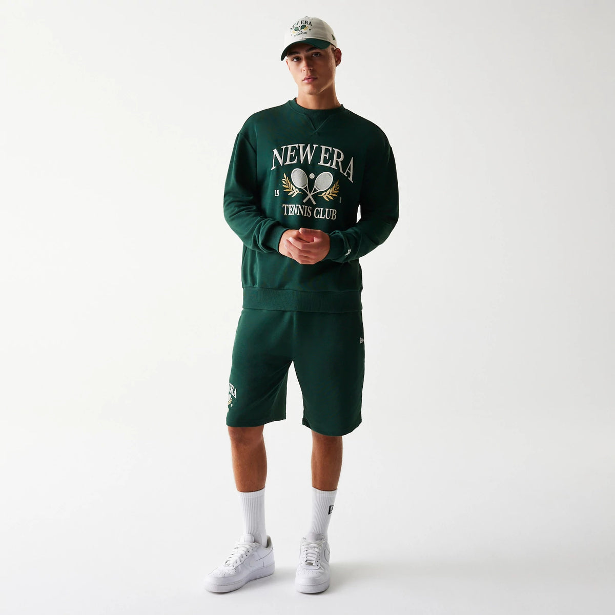 New Era Dark Green Oversized Crew Neck Sweater, front view on a model with matching dark green shorts, featuring large white and gold embroidered New Era Tennis Club graphics across the chest.