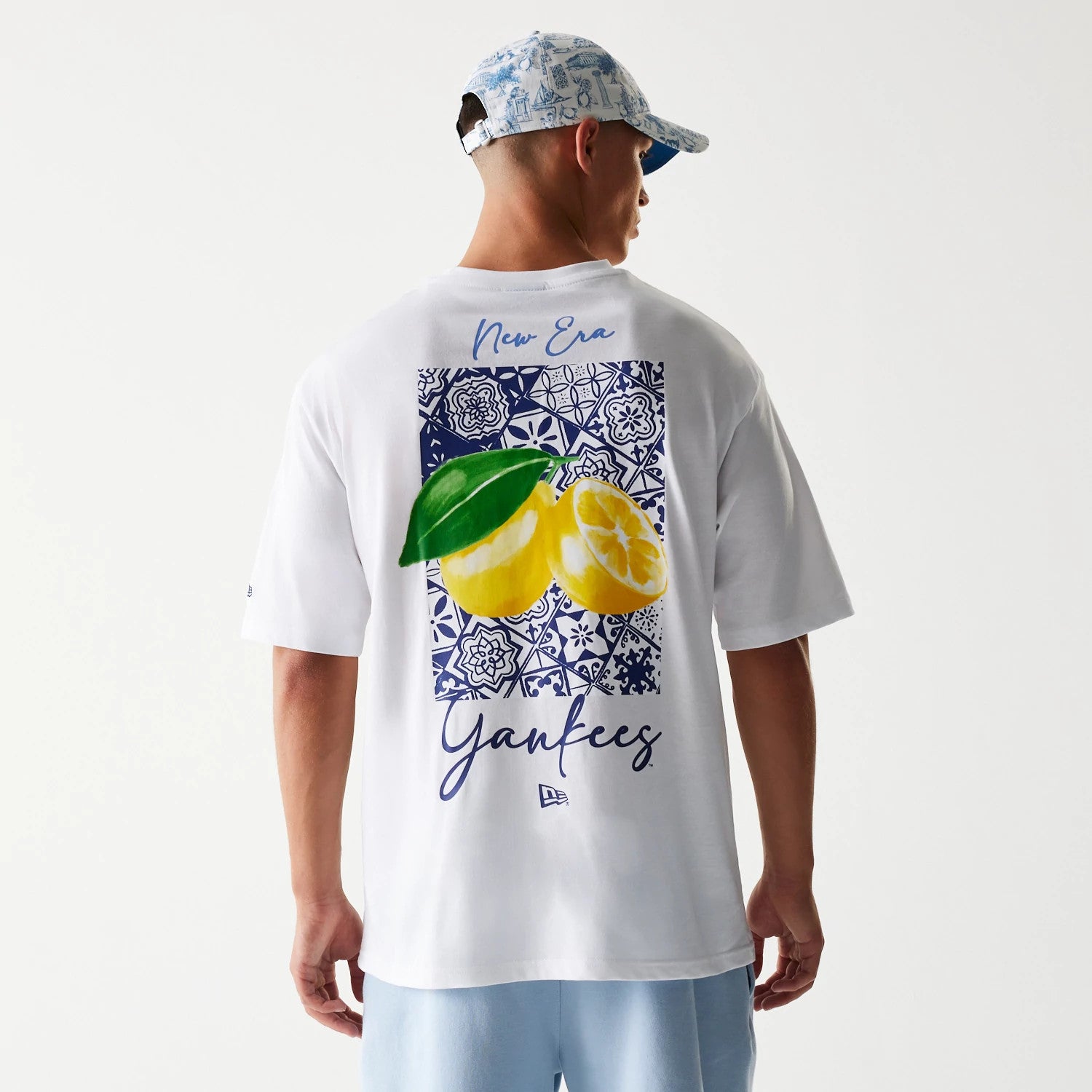 New Era New York Yankees MLB White Oversized T-Shirt, back view showing a blue decorative graphic with lemons and leaves, New Era script across the top, Yankees lettering lower down, and a small printed New Era logo at the bottom.