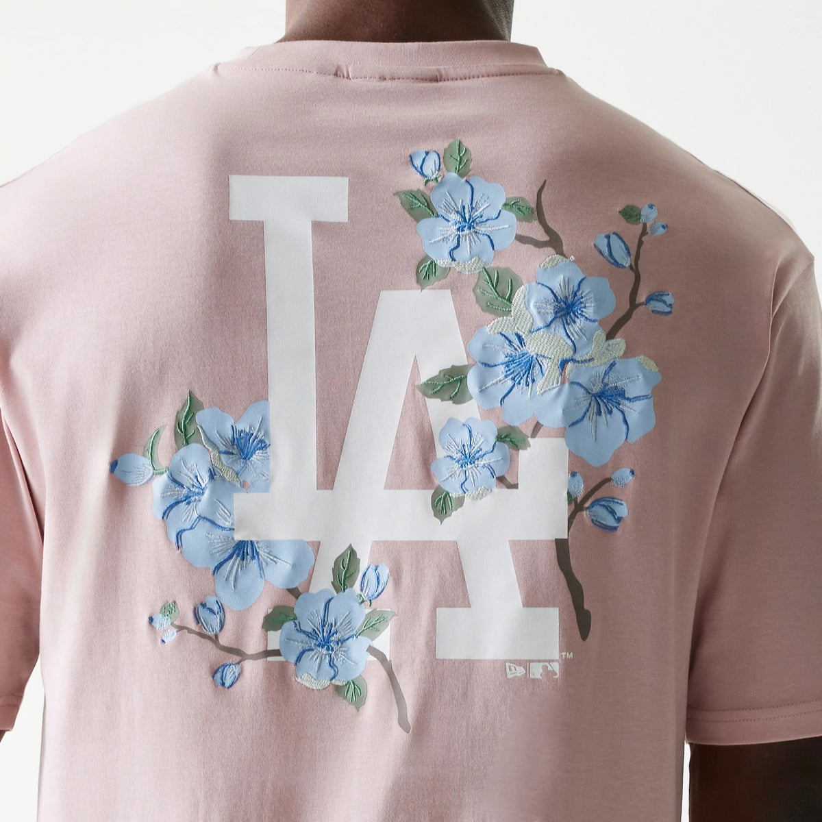 New Era LA Dodgers MLB Floral Pastel Pink Oversized T-Shirt, back view showing a large white LA logo adorned with embroidered blue flowers and green leaves, with the design prominently displayed on the pastel pink fabric.
