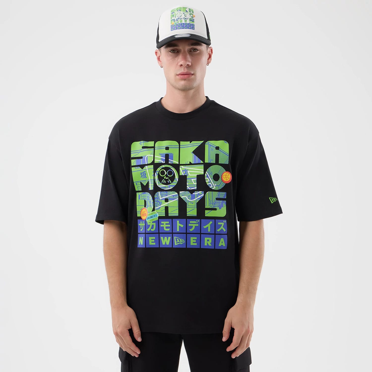 New Era Sakamoto Days Netflix Black T-Shirt, front view showing green and blue graphics featuring text and images across the chest, a small New Era embroidered logo on the sleeve, and styled casually on a model.