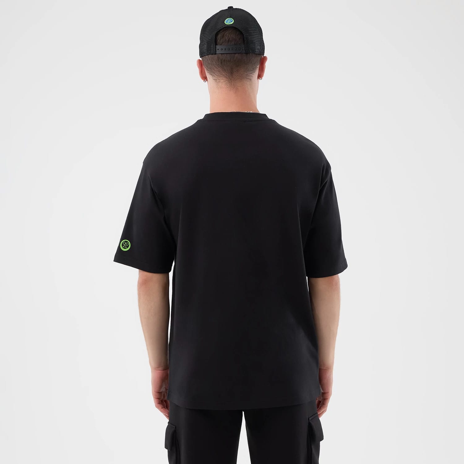 New Era Sakamoto Days Netflix Black T-Shirt, back view on-model showing a black tee with a small green embroidered logo on the left sleeve and a matching black cap with a circular green embroidered logo at the centre back.