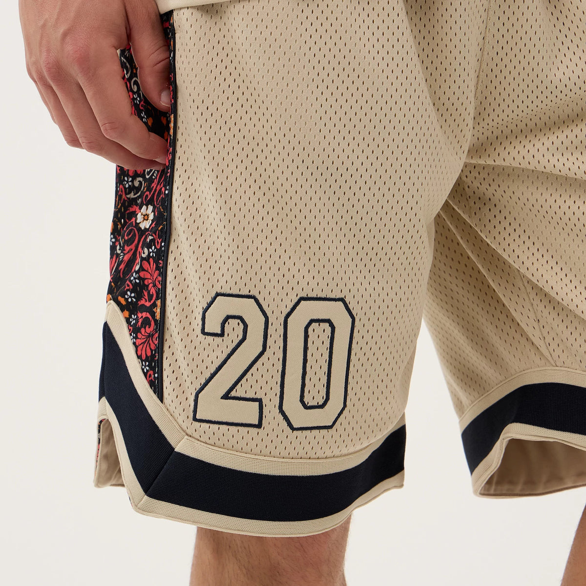 New Era Mesh Light Beige Mesh Shorts, side view featuring the number 20 printed prominently in black on the front right leg, with intricate red and black graphic panels on the sides and a contrasting black trim near the hem.