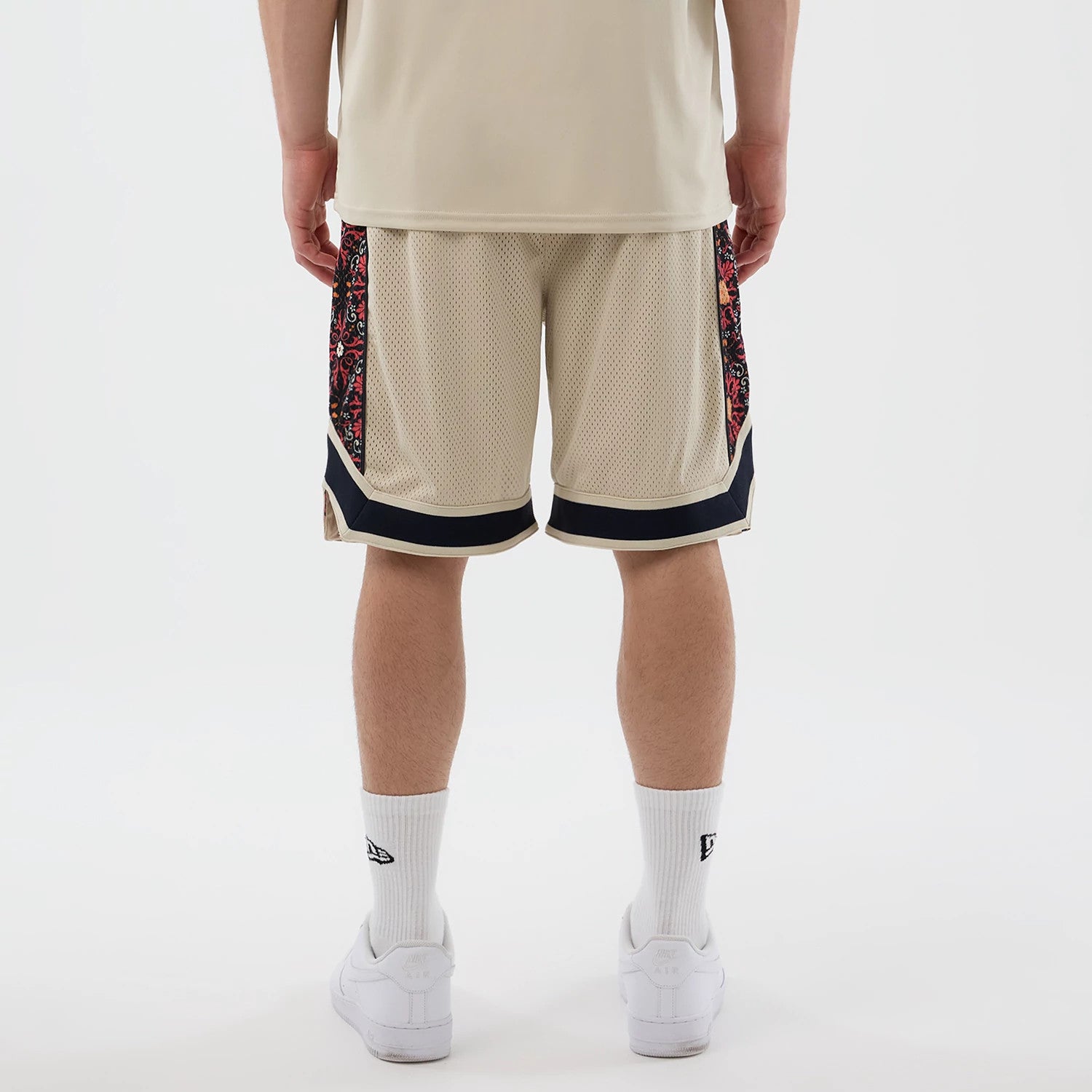 New Era Mesh Light Beige Mesh Shorts, back view on a model showcasing beige mesh fabric with intricate patterned side panels and black trim at the hems, complemented by white socks with an embroidered New Era logo.