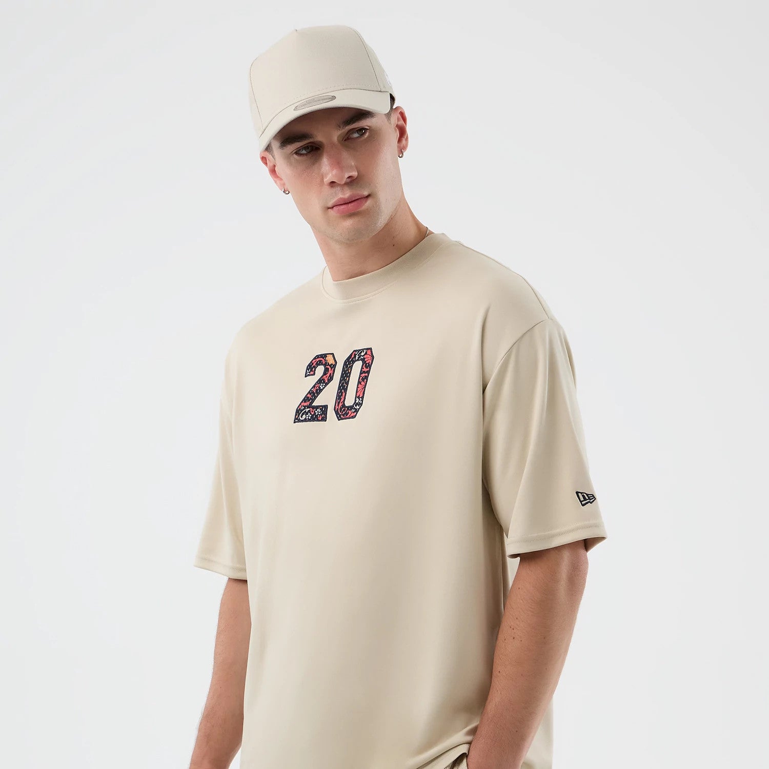 New Era Mesh Infill Light Beige Oversized T-Shirt, front view on a model wearing a matching cap, showcasing a floral-patterned number 20 on the chest and a small embroidered New Era logo on the left sleeve.