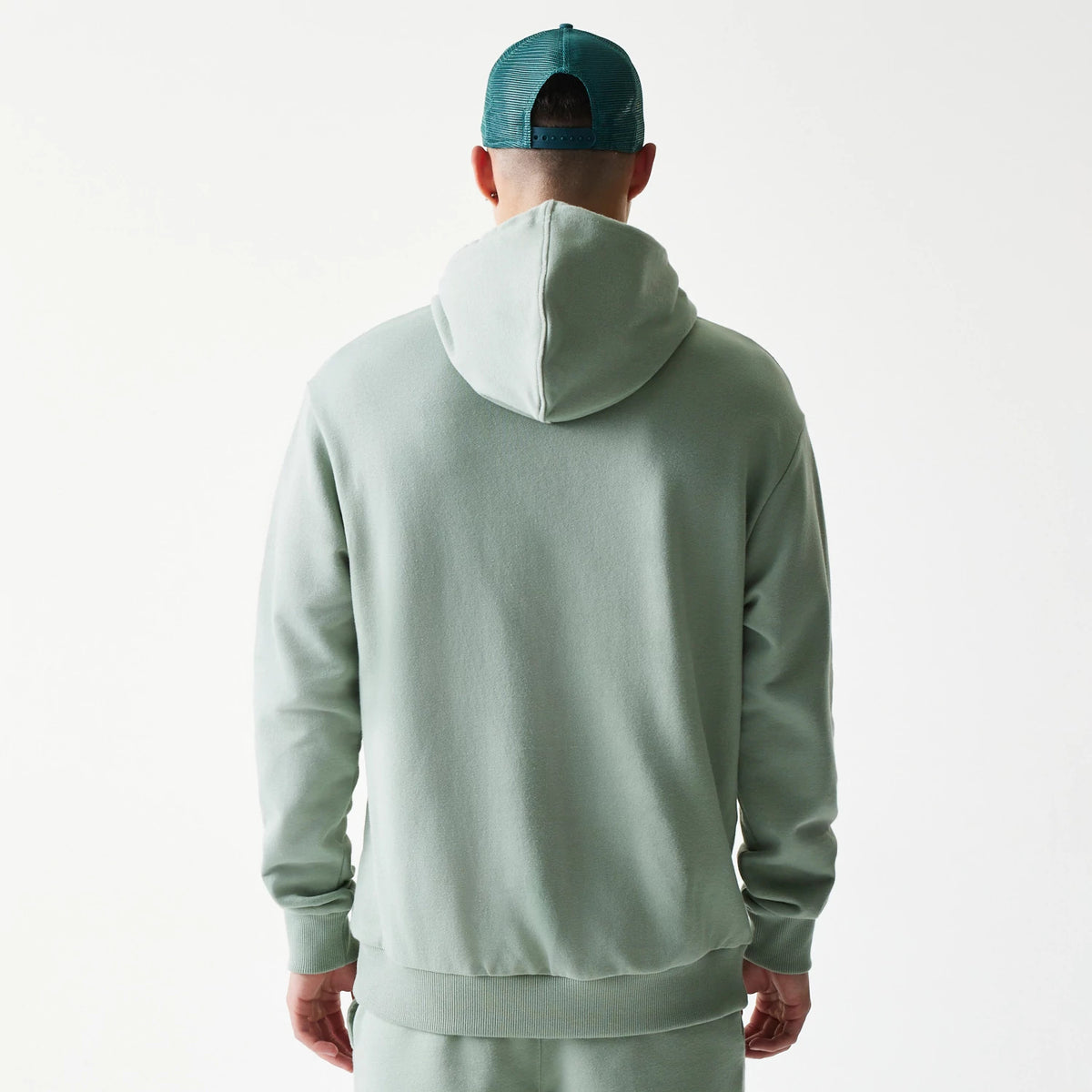 New Era LA Dodgers MLB Midi Pastel Green Oversized Pullover Hoodie, back view on a model showing the relaxed fit with a spacious hood and ribbed cuffs at the wrists, styled with a matching trousers and a dark green cap.
