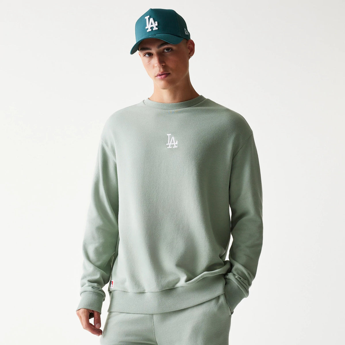 New Era LA Dodgers MLB Midi Pastel Green Oversized Crew Neck Sweater, front view on a model with a white LA logo on the chest and ribbed cuffs, paired with a teal New Era cap featuring an embroidered front LA logo.
