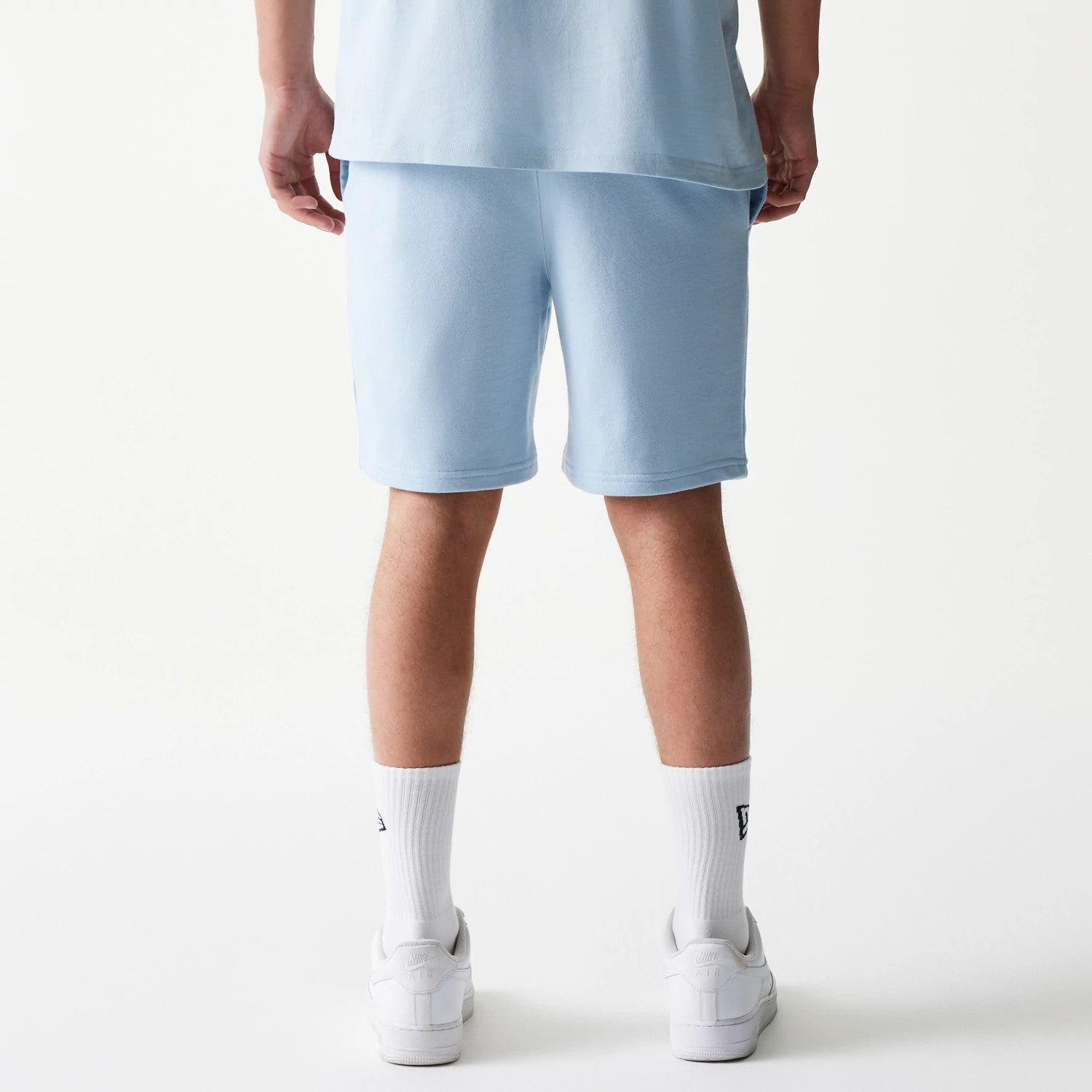 New Era New York Yankees MLB League Essential Midi Pastel Blue Shorts, back view on a model with matching pastel tones, showing the relaxed fit and knee-length cut with along the hem.