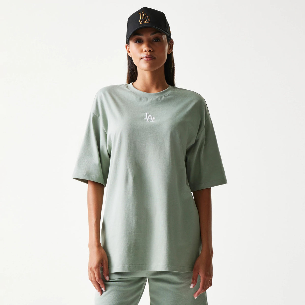 New Era LA Dodgers MLB Midi Pastel Green Oversized T-Shirt, front view on-model showing a relaxed fit with a white embroidered LA logo centred below the neckline, paired with matching pastel green trousers and a black cap.