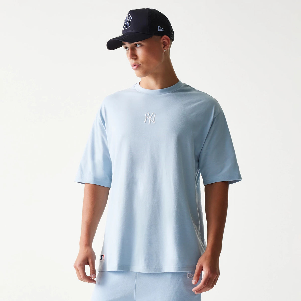 New Era New York Yankees MLB Midi Pastel Blue Oversized T-Shirt, front view on-model showing the white embroidered NY logo centred on the chest, with a relaxed fit and paired with pastel blue shorts and a dark cap.