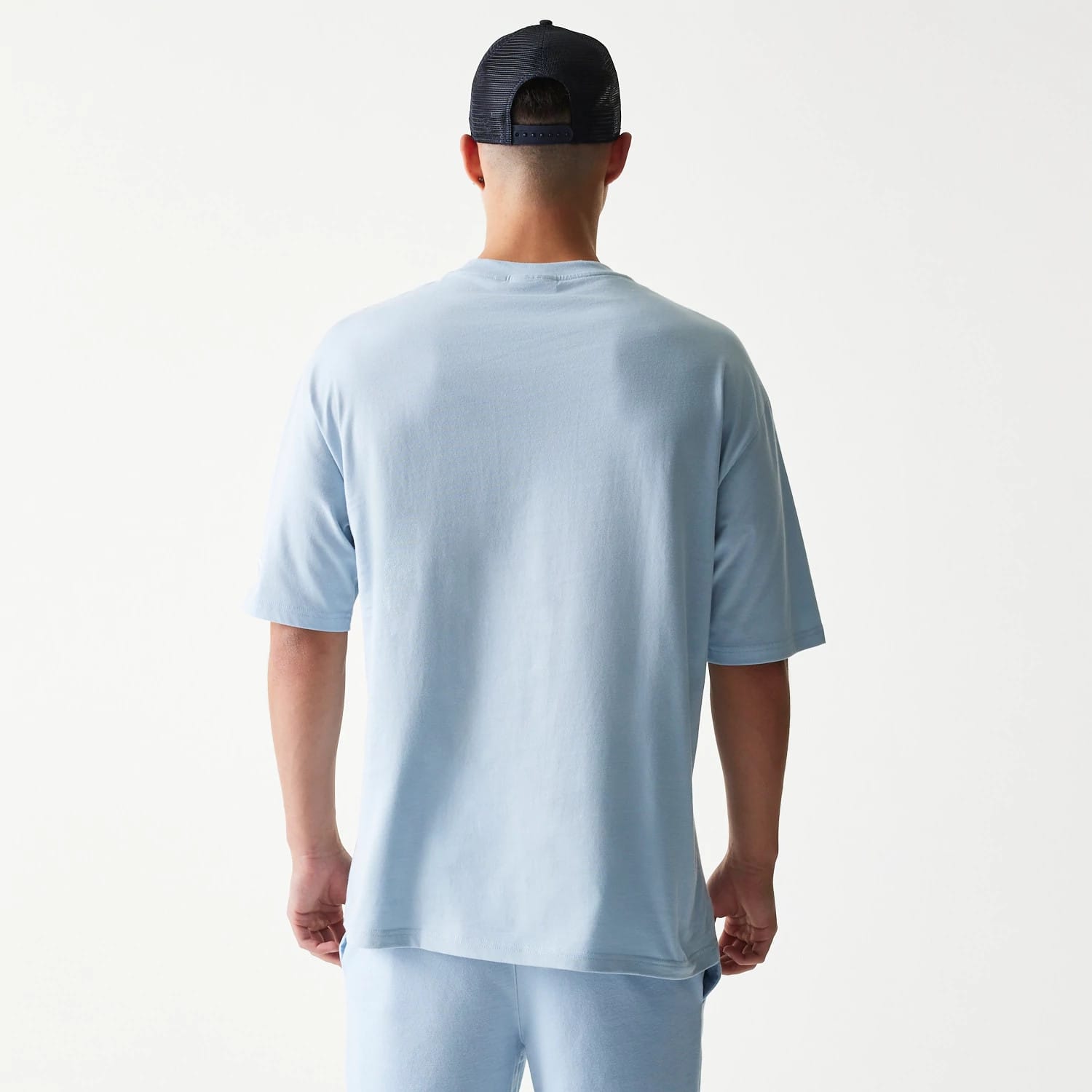 New Era New York Yankees MLB Midi Pastel Blue Oversized T-Shirt, back view on a model wearing a coordinating cap, showing the plain light blue fabric with extended sleeves and a relaxed fit of the oversized design.