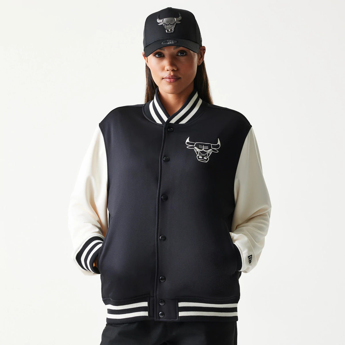 New Era Chicago Bulls NBA Black Bomber Jacket, front view showing the black body with contrasting cream sleeves, embroidered Chicago Bulls logo on the chest, black buttons down the centre, and white-striped ribbed cuffs and collar.