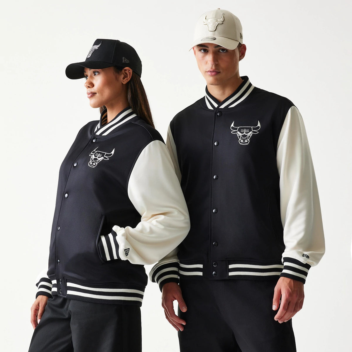 New Era Chicago Bulls NBA Black Bomber Jacket, front view on models styling with caps, featuring a embroidered Bulls logo on the left chest, contrasting cream sleeves, and striped black and white ribbed cuffs and collar.