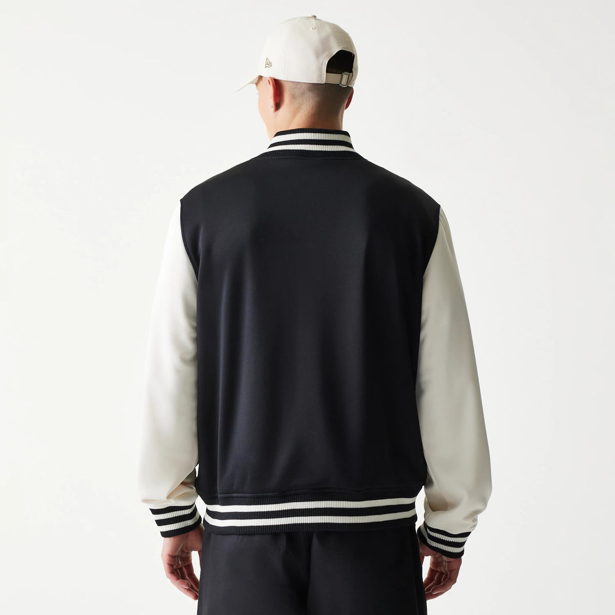 New Era Chicago Bulls NBA Black Bomber Jacket, back view on a model wearing a cream cap, showing black body with cream sleeves, striped ribbed collar, cuffs, and hem for a classic sportswear look.