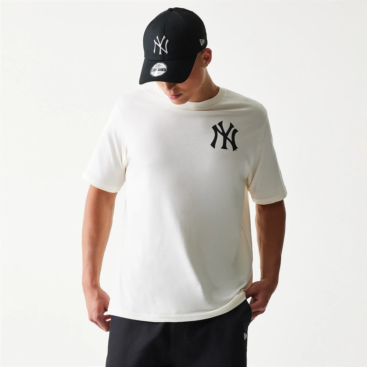 New Era New York Yankees MLB Food Graphic Open White T-Shirt, front view on-model showing the large black embroidered Yankees logo on the chest, paired with a black cap featuring the same logo embroidered on the crown.
