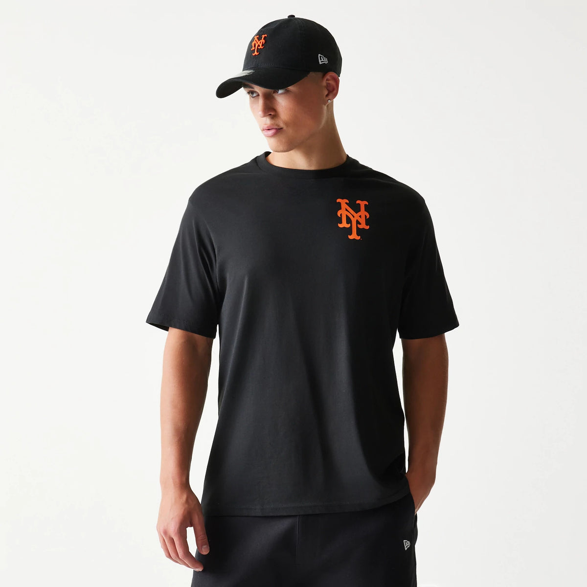 New Era New York Mets MLB Food Graphic Black T-Shirt, front view on-model showing the orange embroidered Mets logo on the left chest with a matching cap featuring the same logo and a raised New Era emblem on the side.