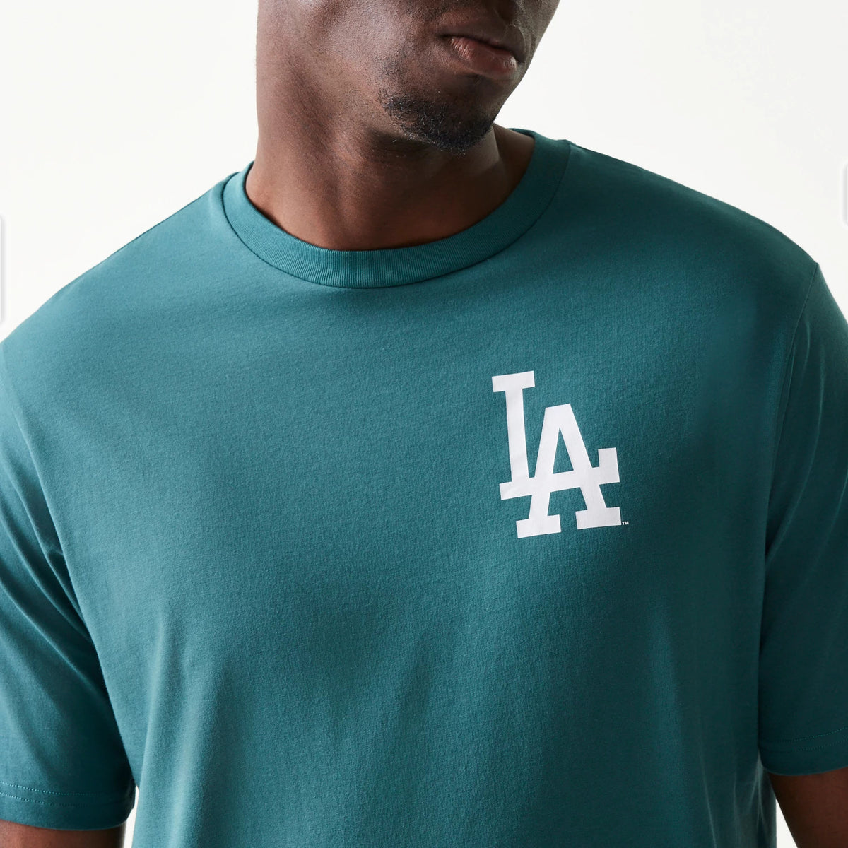 New Era LA Dodgers MLB Food Graphic Dark Green T-Shirt, front view showing the white embroidered LA logo on the left chest, displayed on a model to highlight the classic crew neck and relaxed fit of the dark green tee.