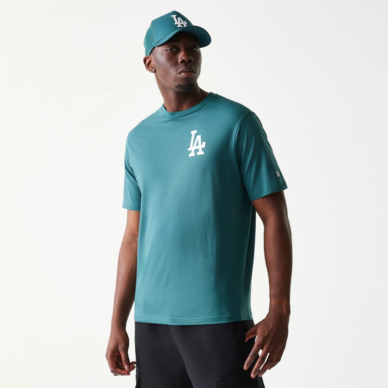 New Era LA Dodgers MLB Food Graphic Dark Green T-Shirt, front view on-model showing a white embroidered LA logo on the left chest, styled with a matching cap and black trousers, capturing a casual look.