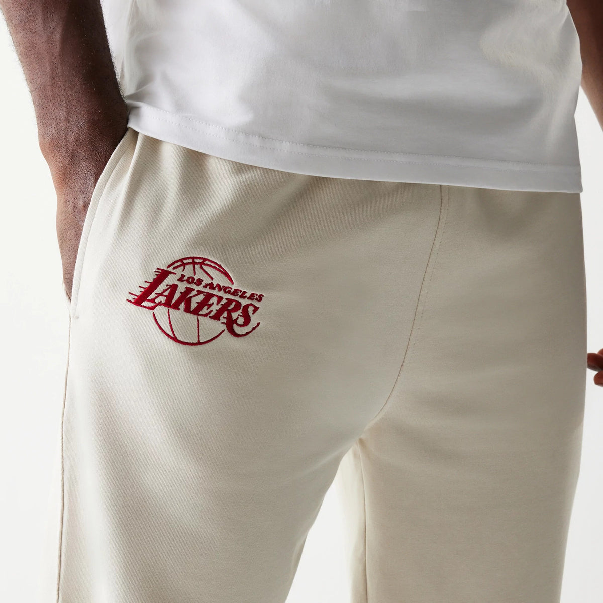 New Era LA Lakers NBA League Essential Cream Joggers, rear view showing a maroon embroidered Los Angeles Lakers logo on the right pocket, with an elastic waistband and a plain cream fabric design.
