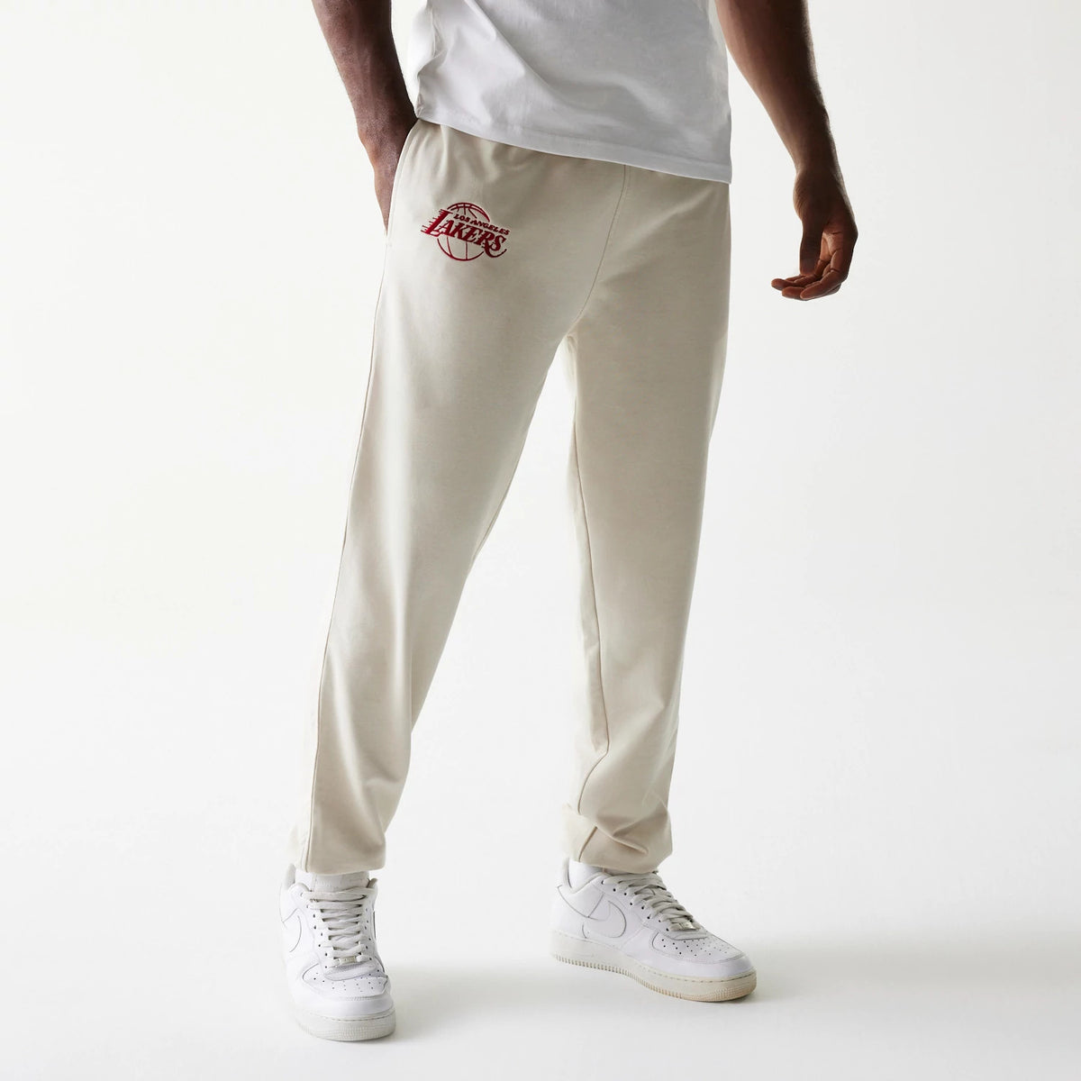 New Era LA Lakers NBA League Essential Cream Joggers, front view on a model wearing white trainers, featuring the red embroidered Lakers logo on the upper left thigh and a straight leg design.