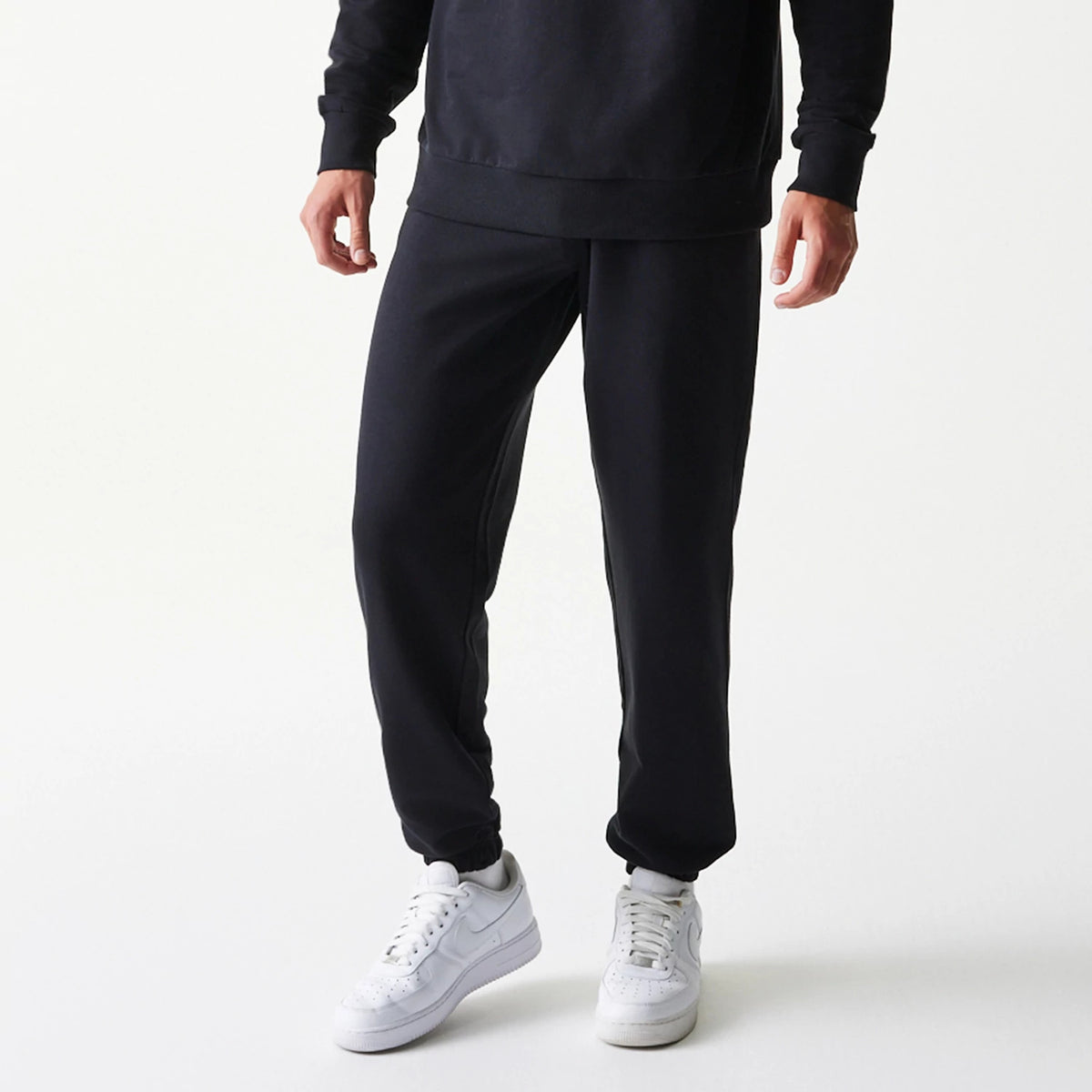 New Era Chicago Bulls NBA League Essential Black Joggers, front view on a model wearing white trainers, showing a relaxed fit with an elastic waistband and ankle cuffs, styled with a matching black top for a casual look.