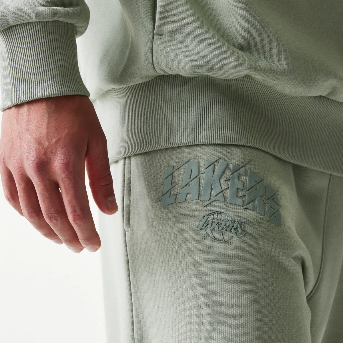 New Era LA Lakers NBA Pastel Green Straight Leg Joggers, side view on a model, showing the Lakers text and logo printed on the upper leg in a matching pastel green, with an elasticated waistband and side pocket detail.