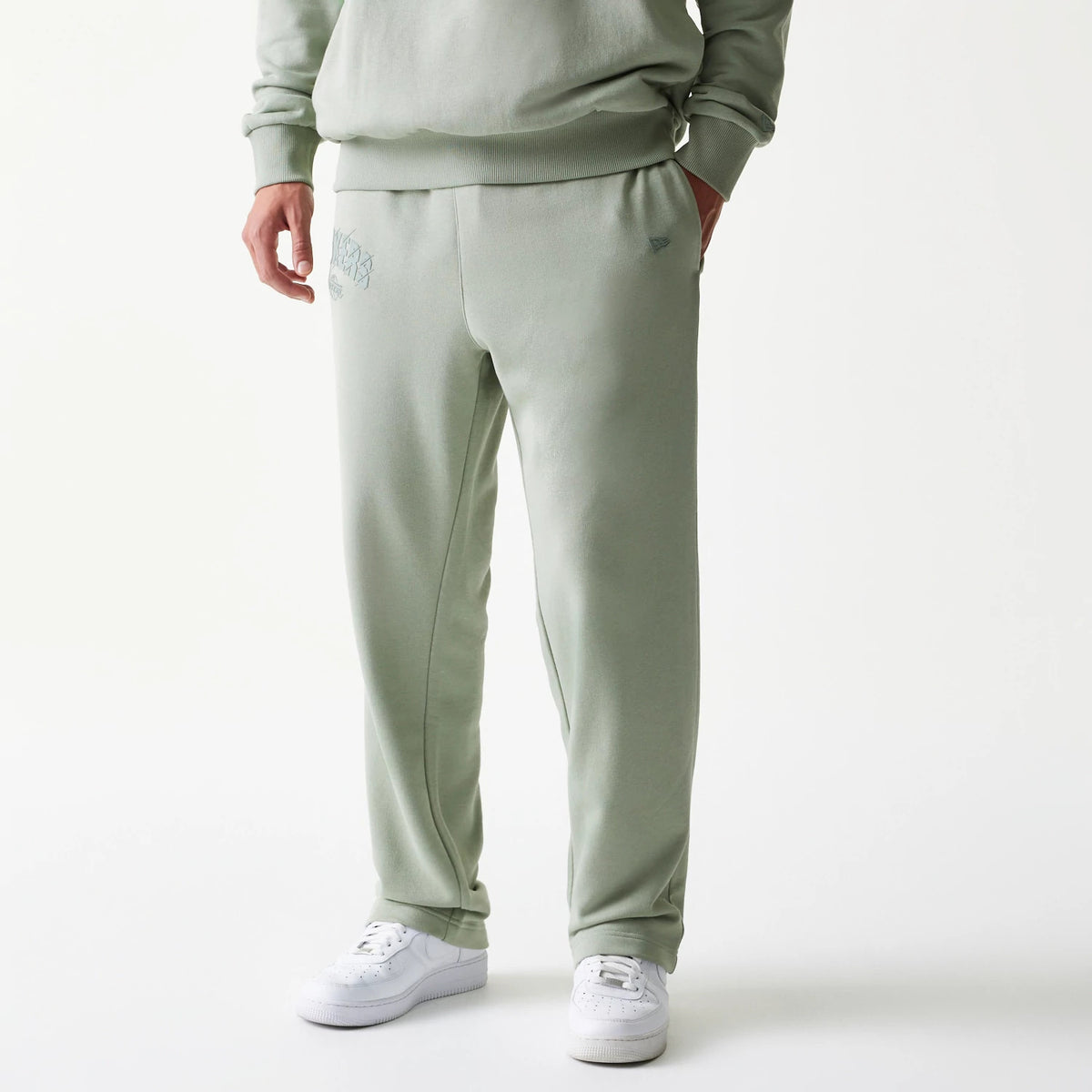 New Era LA Lakers NBA Pastel Green Straight Leg Joggers, front view on a model with hands in pockets, showing the embroidered Lakers logo on the upper left leg and a tidy finish around the ankles, paired with white trainers.