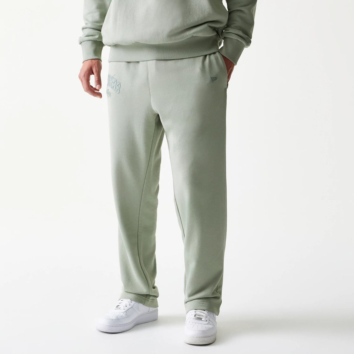 New Era LA Lakers NBA Pastel Green Straight Leg Joggers, front view on a model with hands in pockets, showing the embroidered Lakers logo on the upper left leg and a tidy finish around the ankles, paired with white trainers.