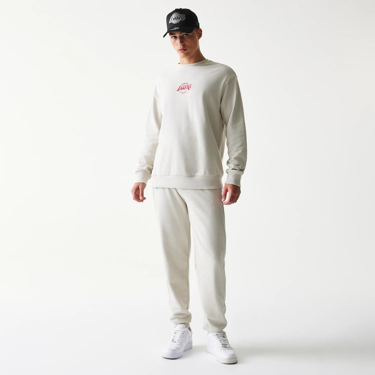 New Era LA Lakers NBA Cream Oversized Crew Neck Sweater, front view on a model with a matching cap, featuring a red Lakers logo embroidered on the chest and ribbed cuffs and hem for a relaxed fit.