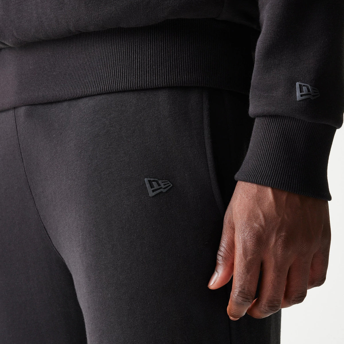New Era Chicago Bulls NBA Black Straight Leg Joggers, close-up view showing the New Era flag logo on the left thigh and the ribbed elastic waistband and cuffs, highlighting the soft black fabric texture.