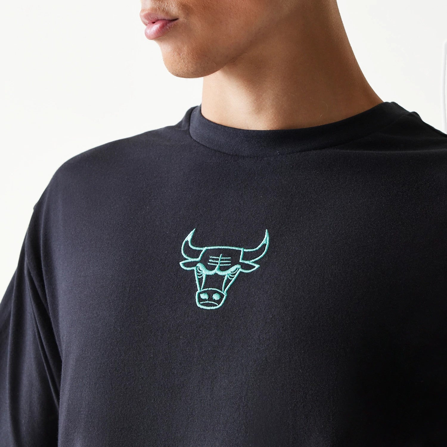 New Era Chicago Bulls NBA League Essential Black Oversized T-Shirt, front view on-model showing a light blue embroidered Bulls logo centred on the chest, with a close-up look at the rounded neckline and slightly loose fit.