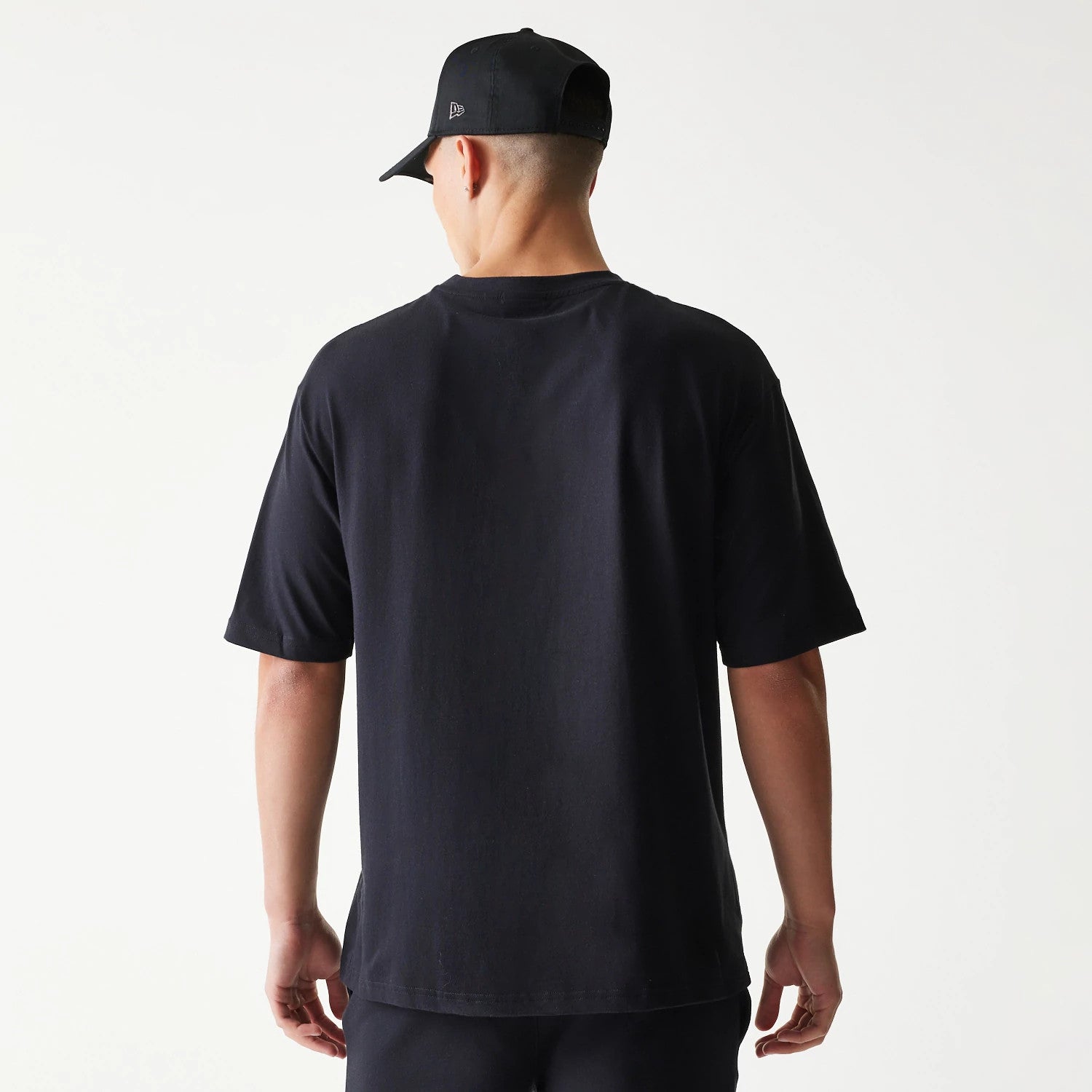 New Era Chicago Bulls NBA League Essential Black Oversized T-Shirt, back view on a model with a simple design featuring plain black fabric, short sleeves, and complemented by a black cap with a small embroidered New Era logo on the side.