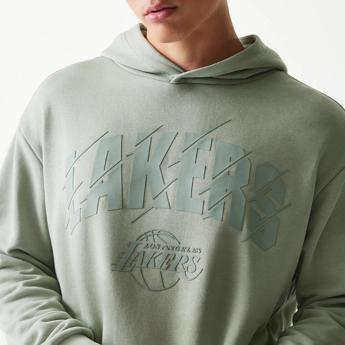 New Era LA Lakers NBA Pastel Green Oversized Pullover Hoodie, front view showing large raised Lakers lettering across the chest with a smaller debossed Lakers logo and basketball graphic below, worn by a model with the hood down.