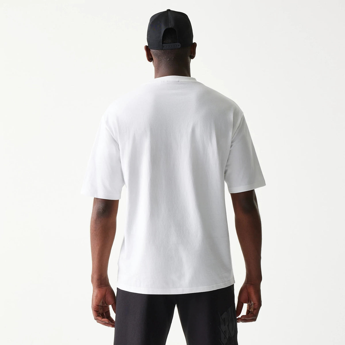 New Era Chicago Bulls NBA White Oversized T-Shirt, back view on a model with black shorts and a black cap, showcasing the plain white back of the oversized T-shirt and simple short sleeves.
