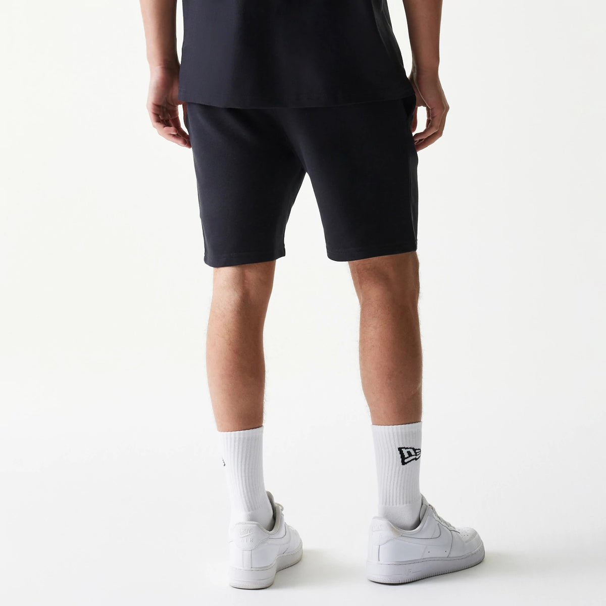 New Era Chicago Bulls NBA League Essential Black Shorts, back view on a model wearing white socks and trainers, showing the simple black design with elastic waistband and mid-thigh length for a classic look.