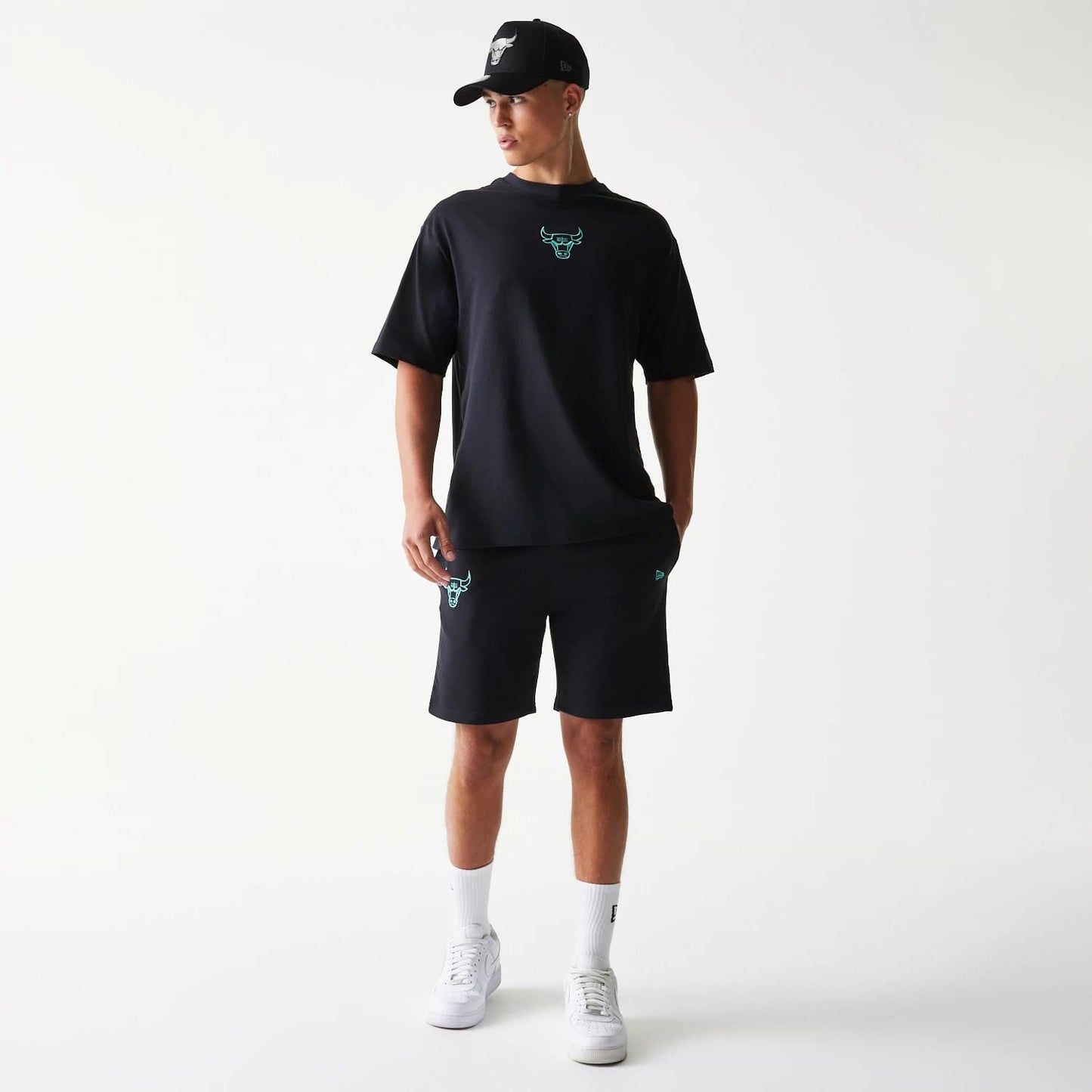 New Era Chicago Bulls NBA League Essential Black Shorts, on-model front view showing the teal embroidered Bull logo on the left leg and the black colourway, styled with a matching black t-shirt with a teal logo on the chest and a black cap.