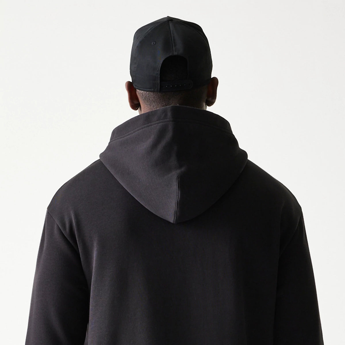 New Era Chicago Bulls NBA Black Oversized Pullover Hoodie, back view on a model with a black cap, featuring a plain back with a relaxed hood over the neck, showcasing the simple black design without any graphics or logos.