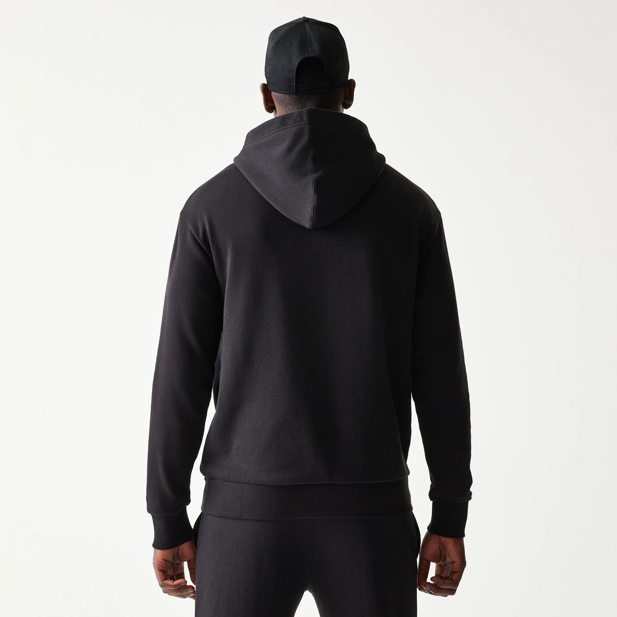 New Era Chicago Bulls NBA Black Oversized Pullover Hoodie, back view on a model with a black cap, showing the plain black hoodie with a relaxed fit and a large hood draped at the neckline.