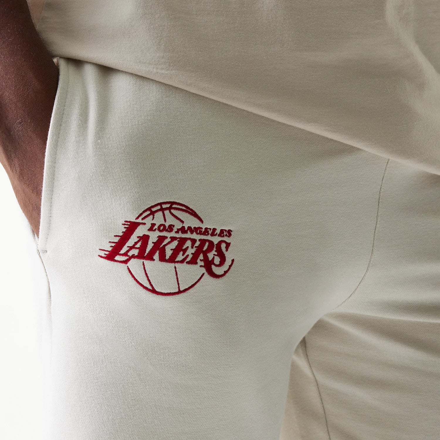 New Era LA Lakers NBA League Essential Cream Shorts, close-up front view showing the embroidered red Los Angeles Lakers logo with basketball design on the left leg, styled casually with a matching cream top.
