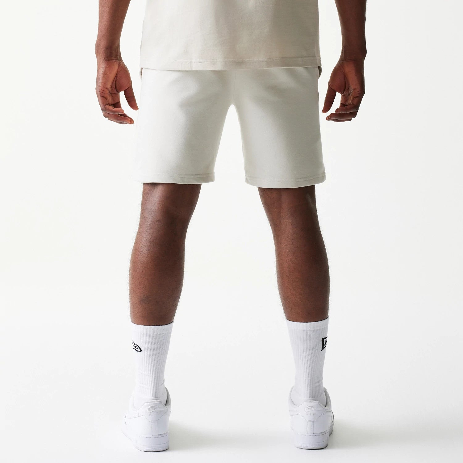 New Era LA Lakers NBA League Essential Cream Shorts, back view on a model showing the plain cream design with an elastic waistband, styled with white socks and trainers for a casual look.