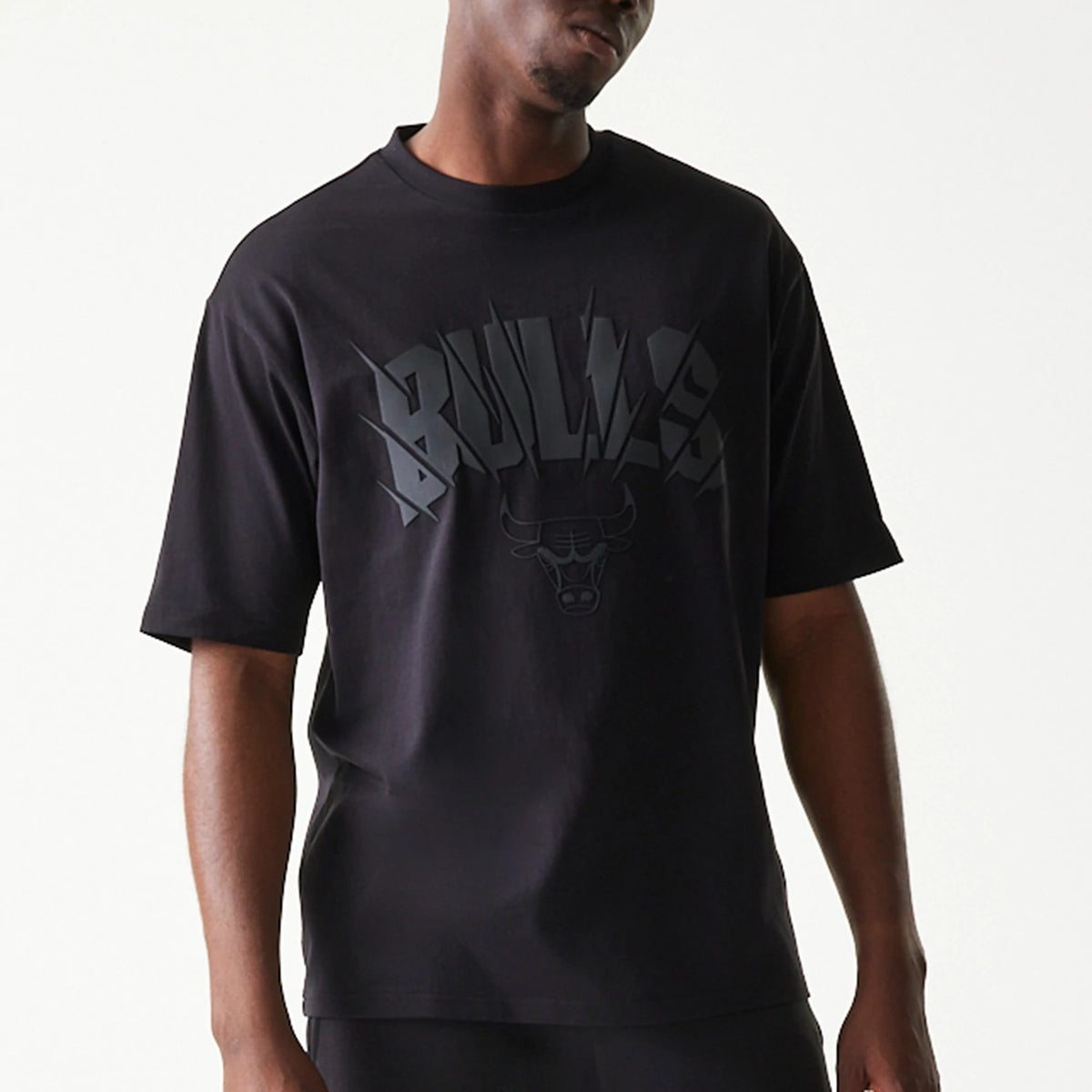 New Era Chicago Bulls NBA Black Oversized T-Shirt, front view on-model featuring large black Bulls graphic and logo across the chest, short sleeves, and a round neckline, styled with black trousers.