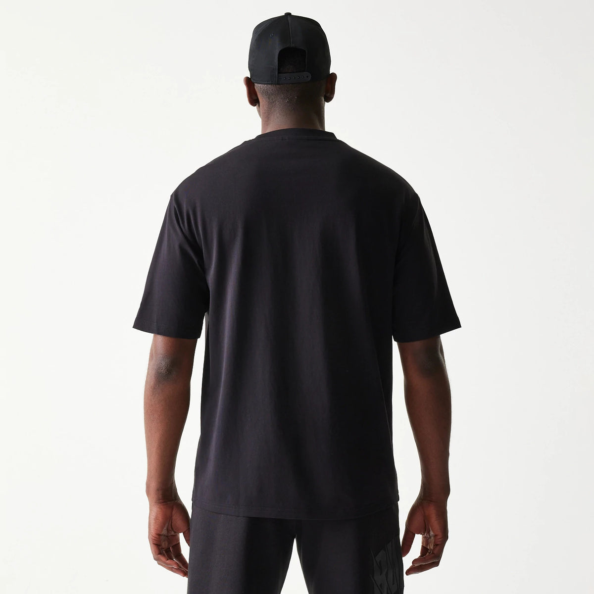 New Era Chicago Bulls NBA Black Oversized T-Shirt, back view on a model paired with shorts and a cap, showing a plain black back with no logos or graphics, emphasising the relaxed oversized fit.