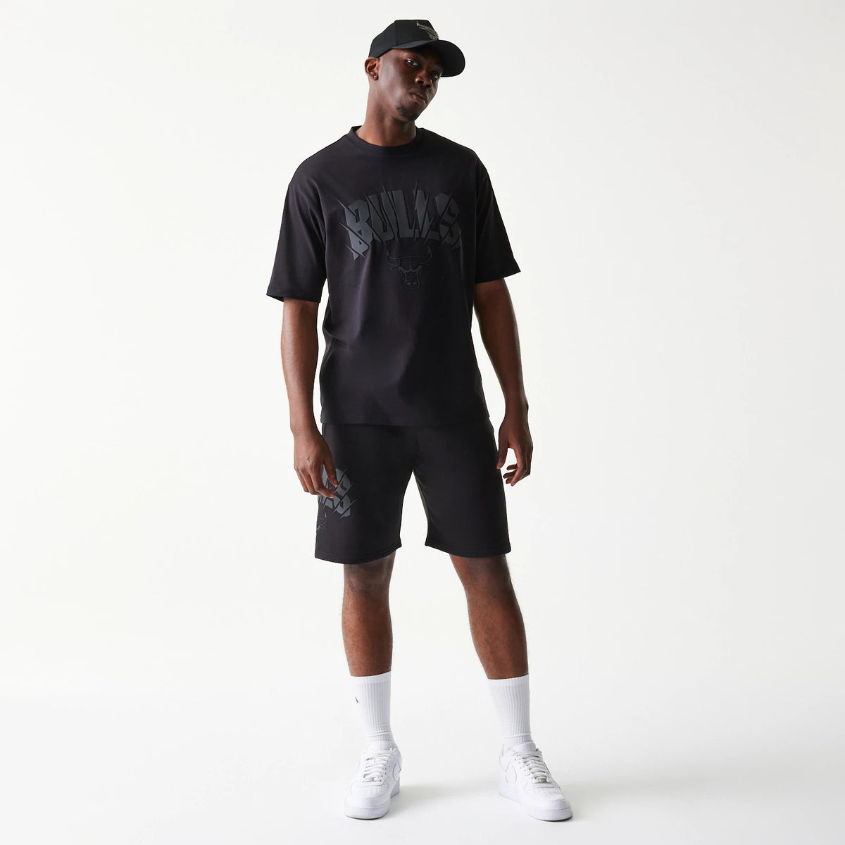 New Era Chicago Bulls NBA Black Oversized T-Shirt, front view on-model displaying Bulls lettering and logo in dark grey on the chest, paired with matching black shorts and a cap, highlighting a casual sporty look.