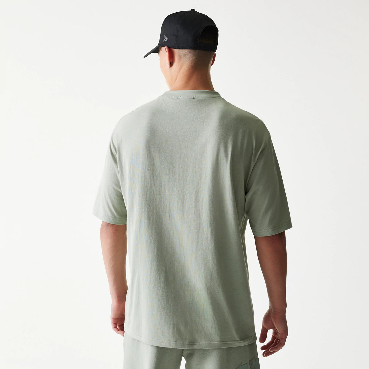 New Era LA Lakers NBA Pastel Green Oversized T-Shirt, back view on model wearing a black cap, showing a plain pastel green back panel and short sleeves, styled with matching coloured shorts for a coordinated look.
