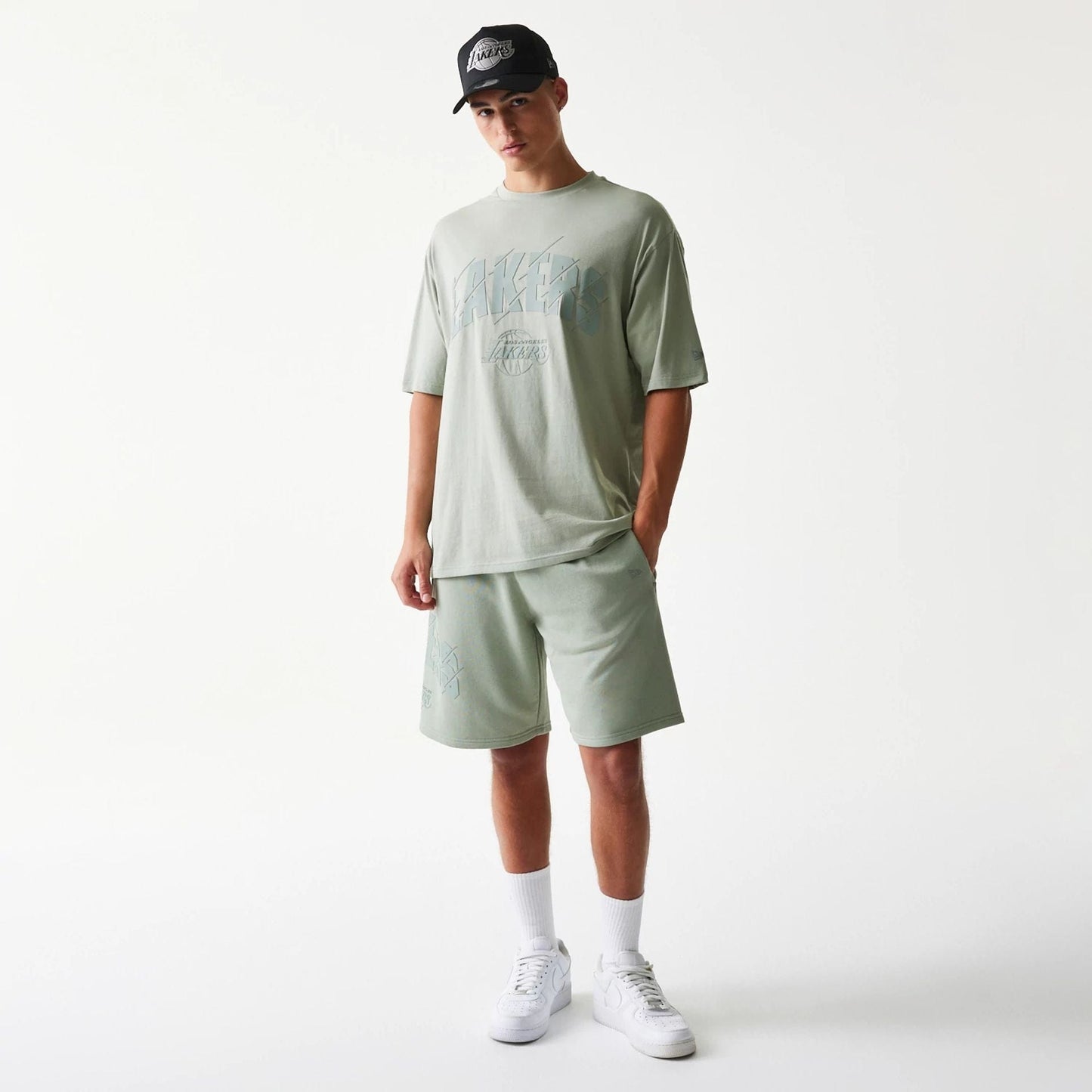 New Era LA Lakers NBA Pastel Green Oversized T-Shirt, front view on-model showing the Lakers logo printed in blue across the chest, styled with pastel green shorts and a black cap featuring an embroidered Lakers emblem.